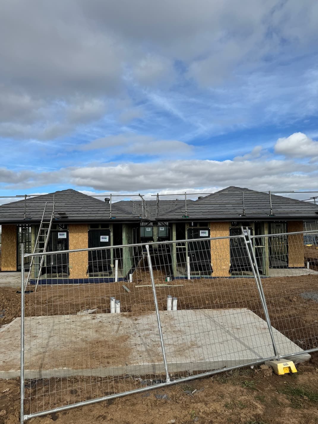 A newly constructed one-story building under a blue sky, surrounded by a metal security fence and construction debris.