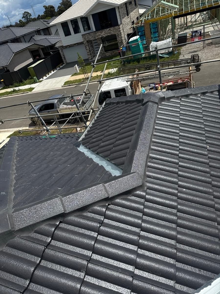 A high-angle view of a newly tiled grey roof with a valley gutter, with a residential construction site in the background.