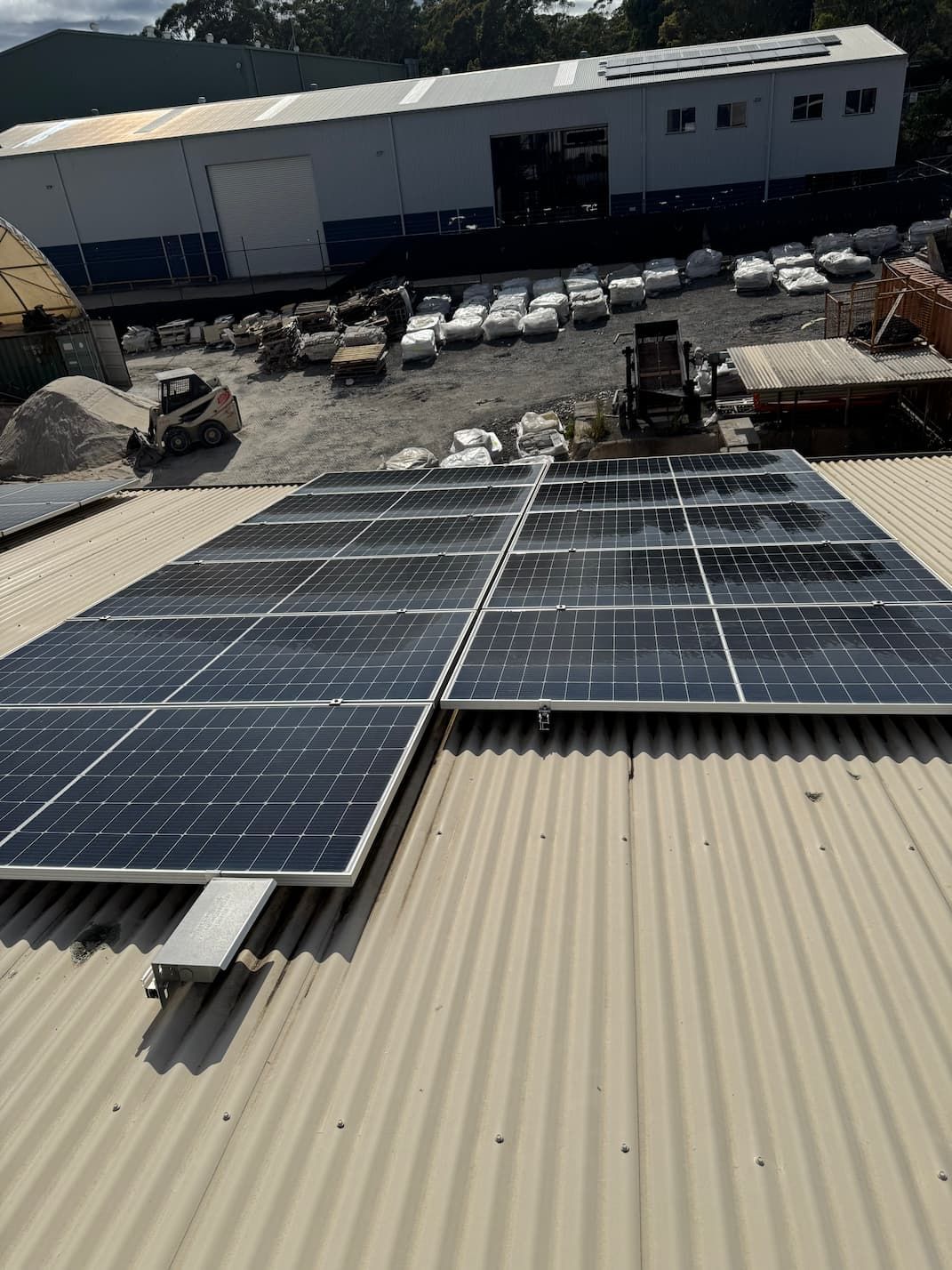 Solar panels installed on a corrugated metal roof, overlooking a construction site with building materials and machinery.