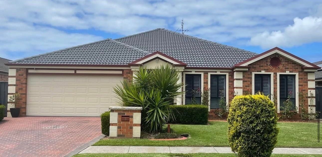 A single-story brick house with a double garage, a tiled roof, and a front garden on a sunny day.