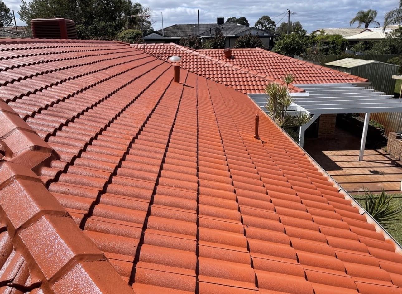 A view of a freshly painted, bright terracotta tiled roof against a clear blue sky on a sunny day.