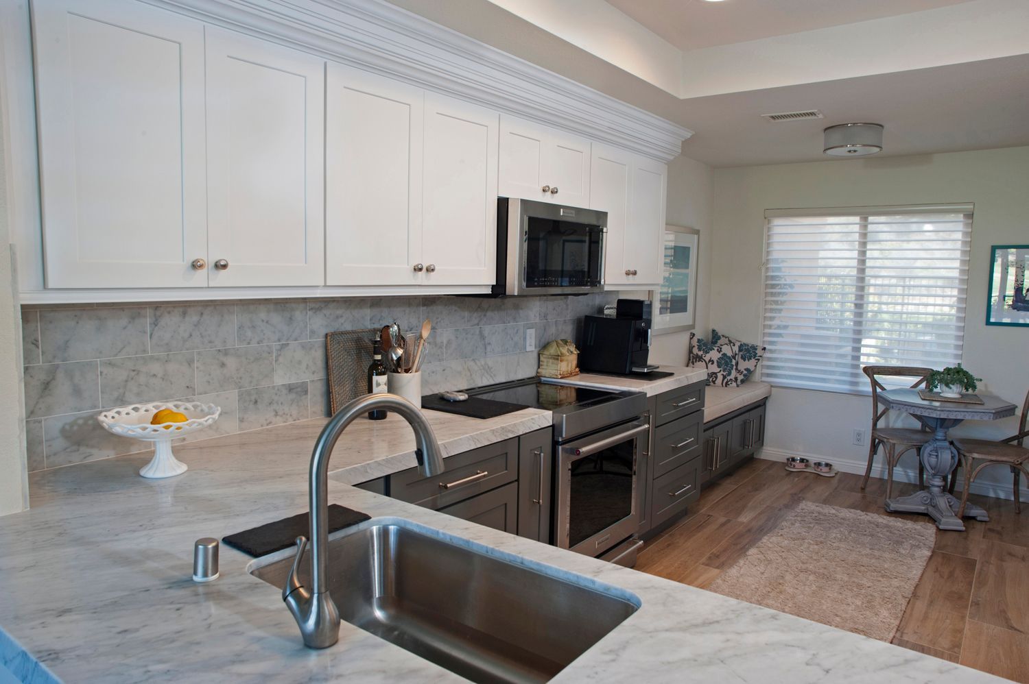 Modern kitchen with white cabinets, gray island, stainless steel appliances, and dining area.