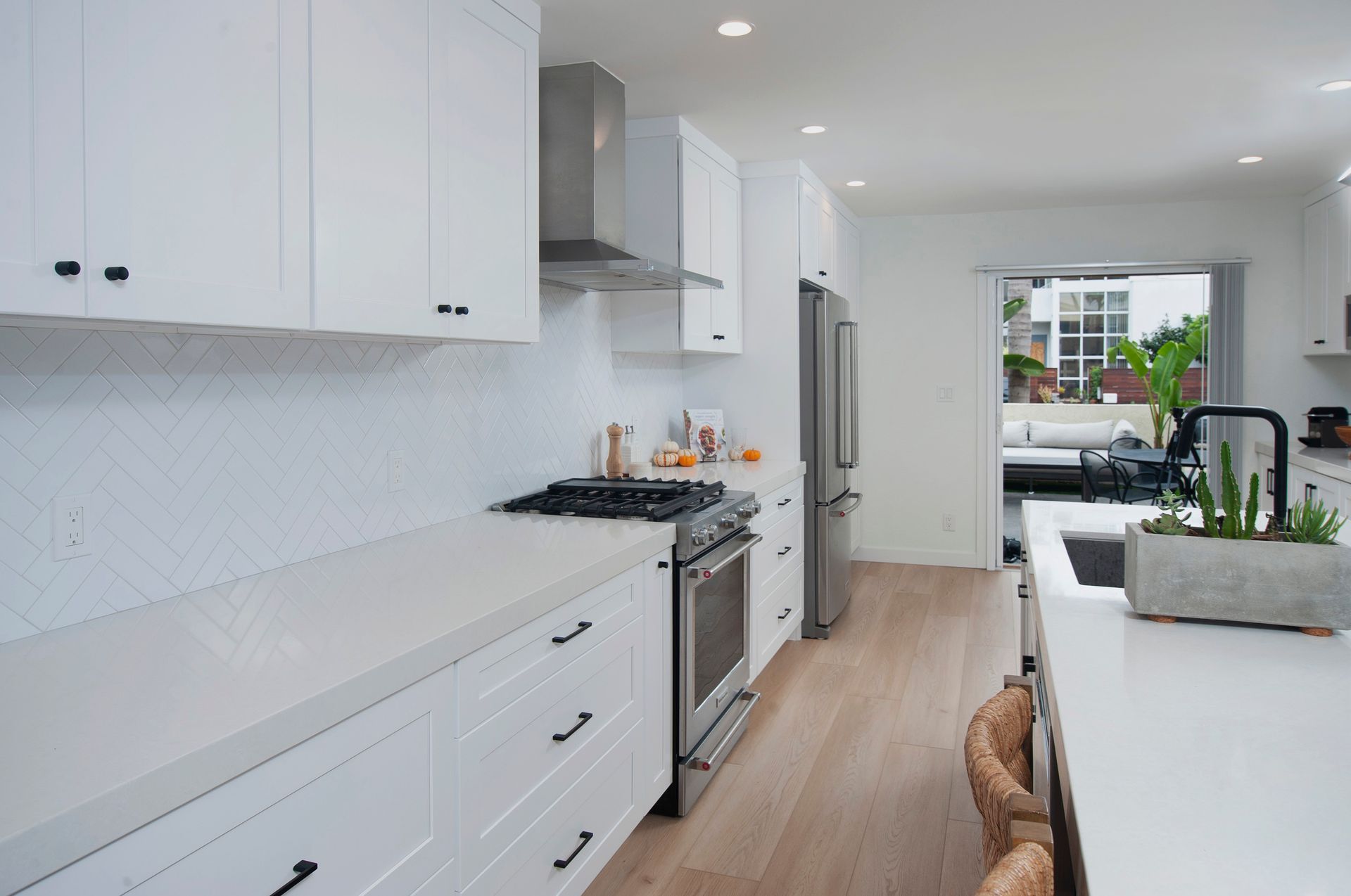 White kitchen with long countertop, cabinets, and stainless steel appliances. Opens to a patio.