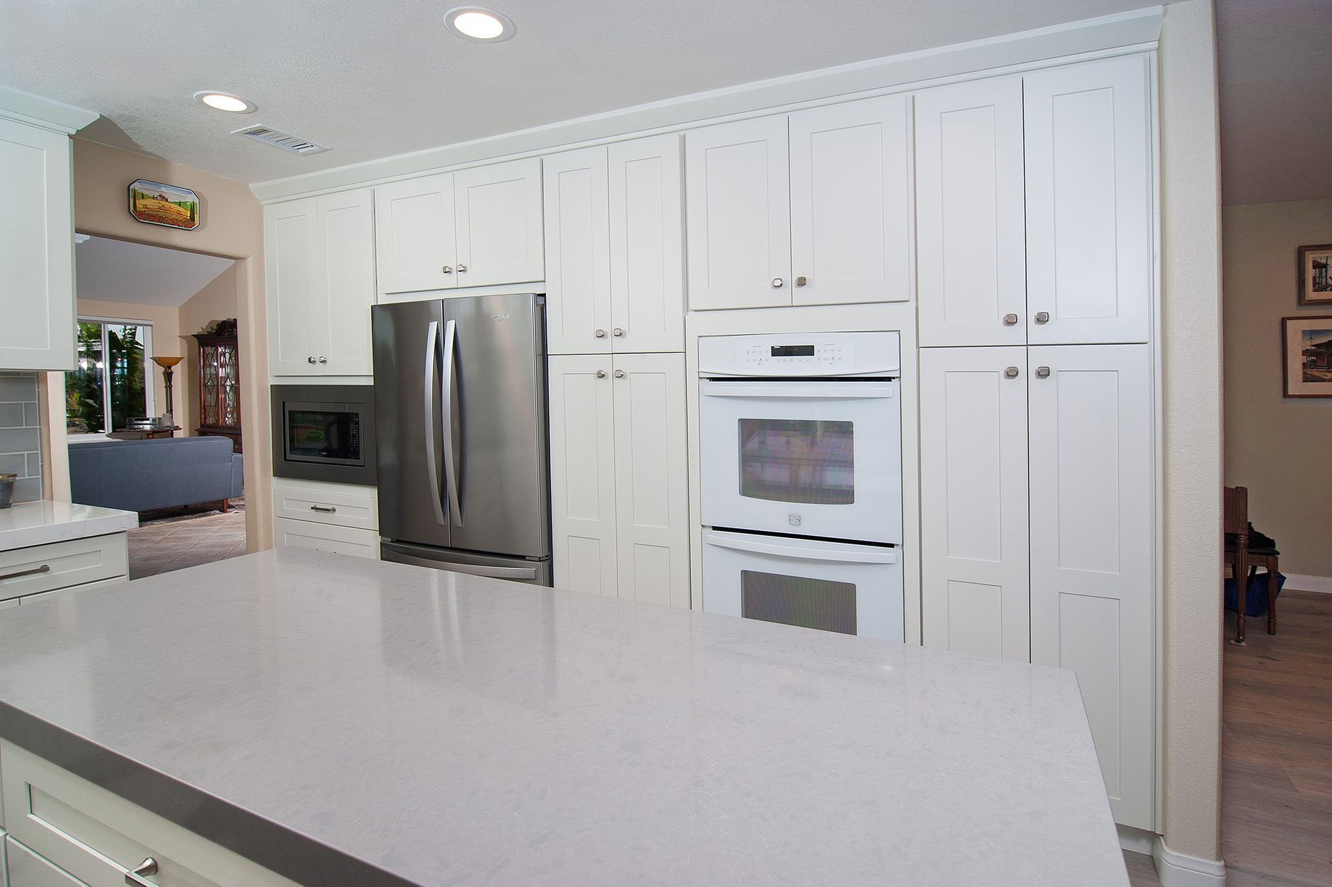 White kitchen with large island and stainless steel refrigerator, oven, and cabinets.