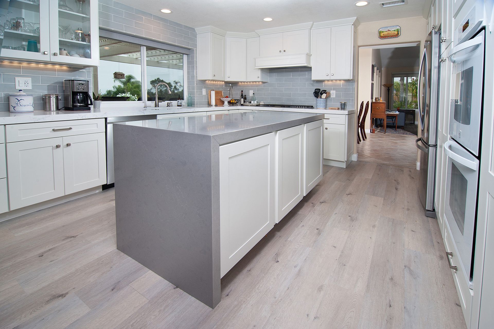 Modern kitchen with white cabinets, gray island, light wood floors, and stainless steel appliances.