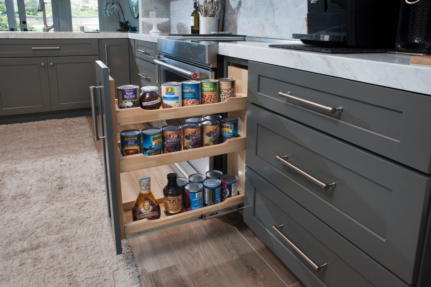 Pull-out pantry with shelves of canned goods, spices, and bottles in a gray kitchen cabinet.