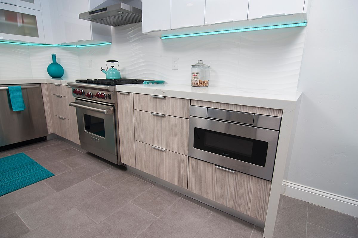 Modern kitchen with stainless steel appliances, light wood cabinets, and turquoise accents.