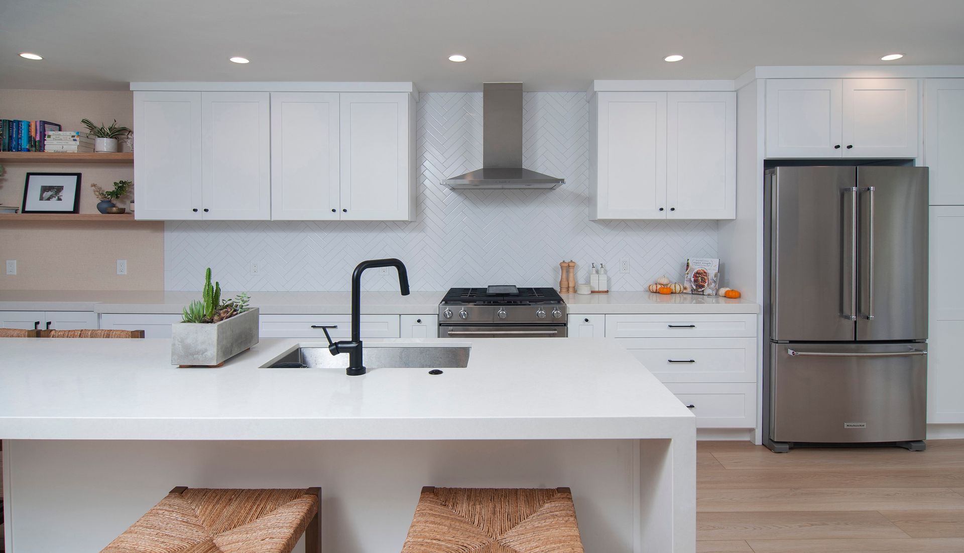 Modern white kitchen with stainless steel appliances, island with sink and black faucet.