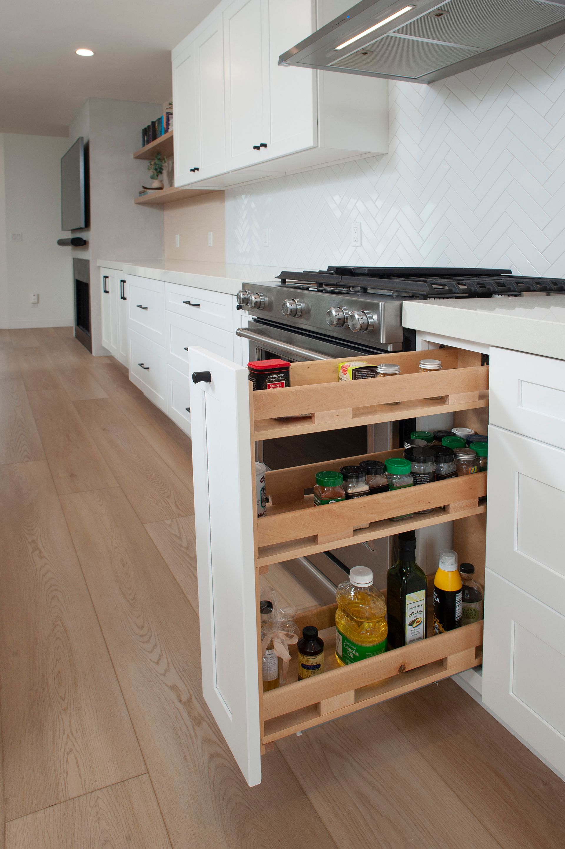 White kitchen with pull-out spice rack. Light wood floors, white cabinets, countertop, and backsplash.