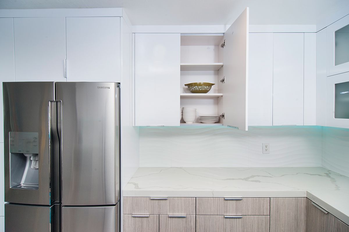 Stainless steel refrigerator next to white kitchen cabinets, one cabinet door open showing dishes.