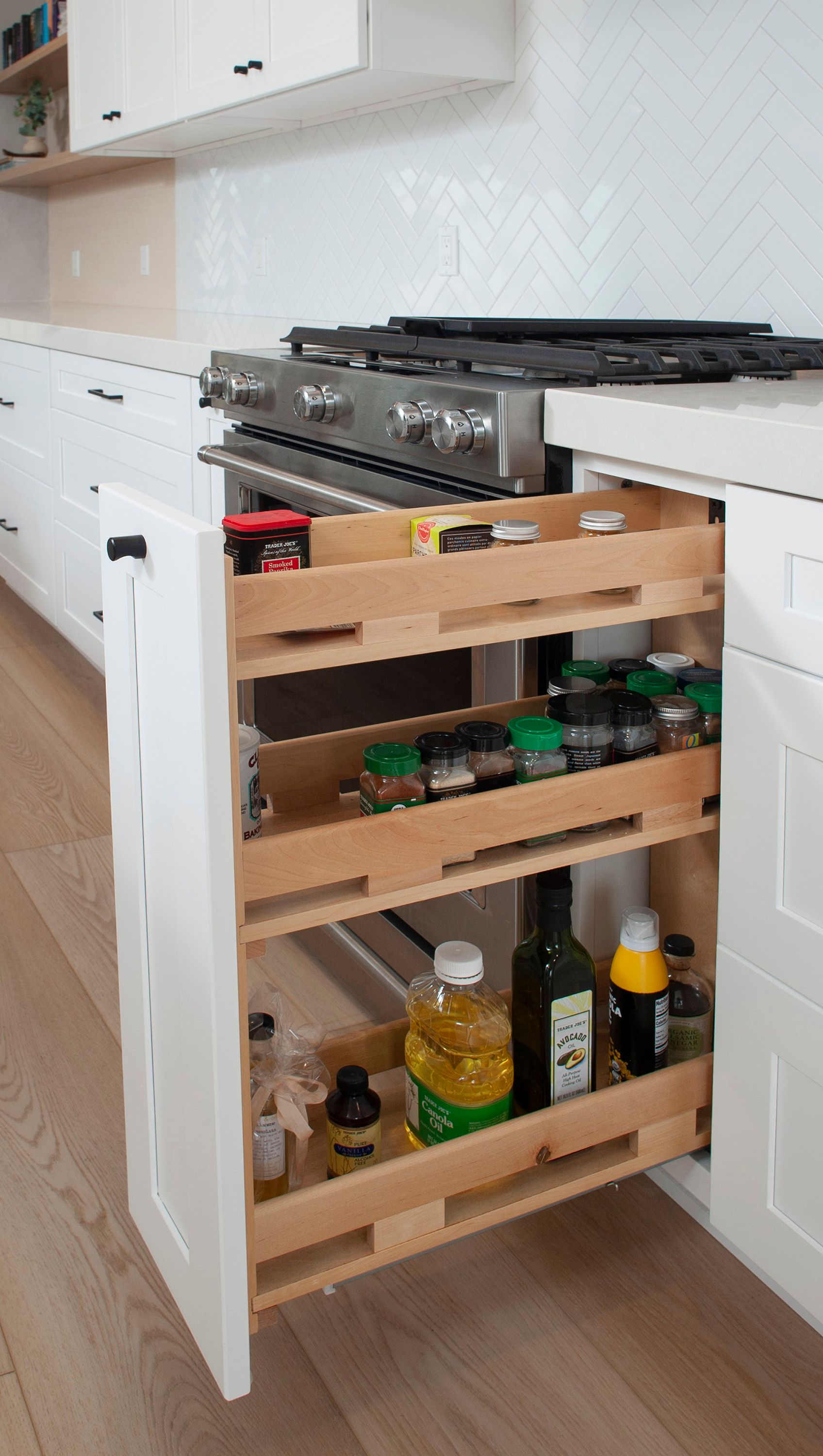 Pull-out spice rack in a white kitchen filled with spices, oils, and other cooking essentials.