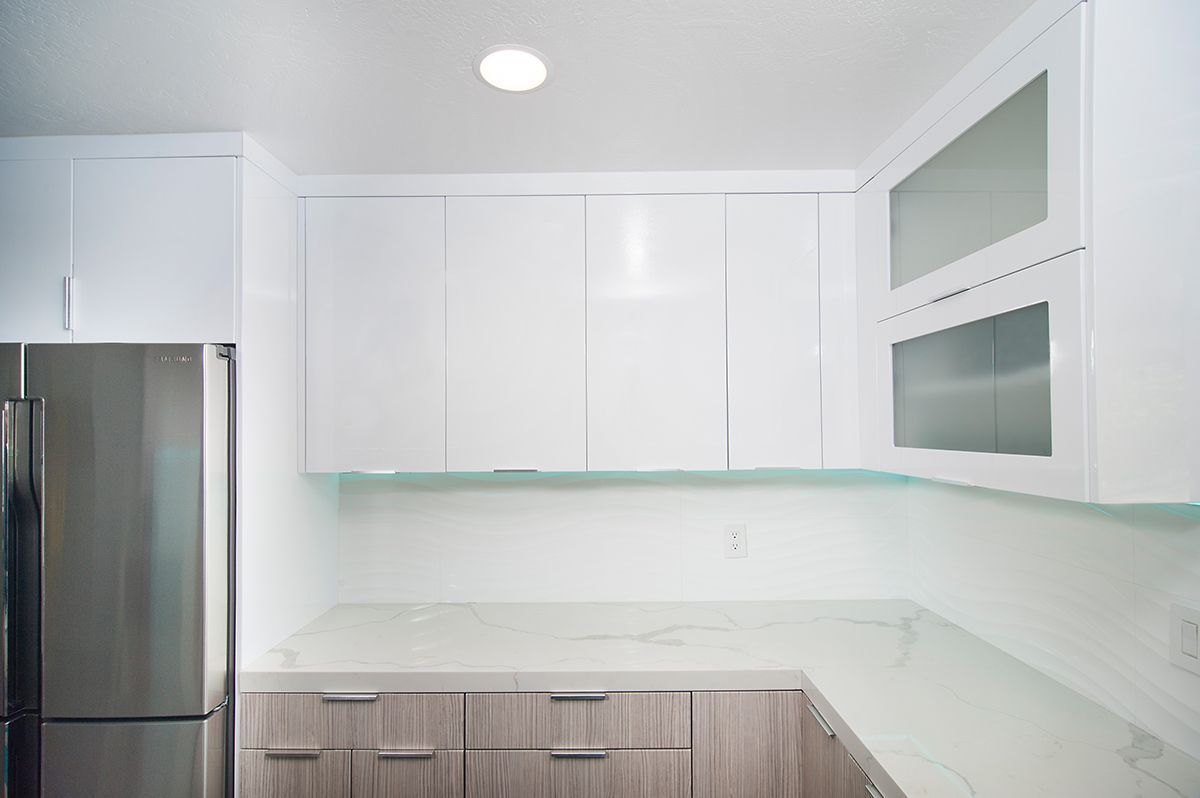 White and wood-toned kitchen with stainless steel fridge, white cabinets, and countertop.