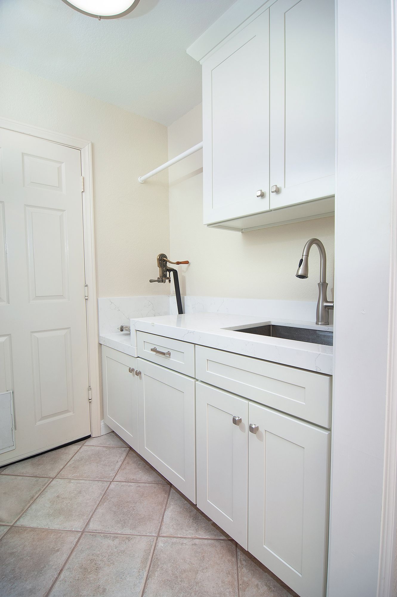 Laundry room with white cabinets, sink, and tile floor. Door on the left.