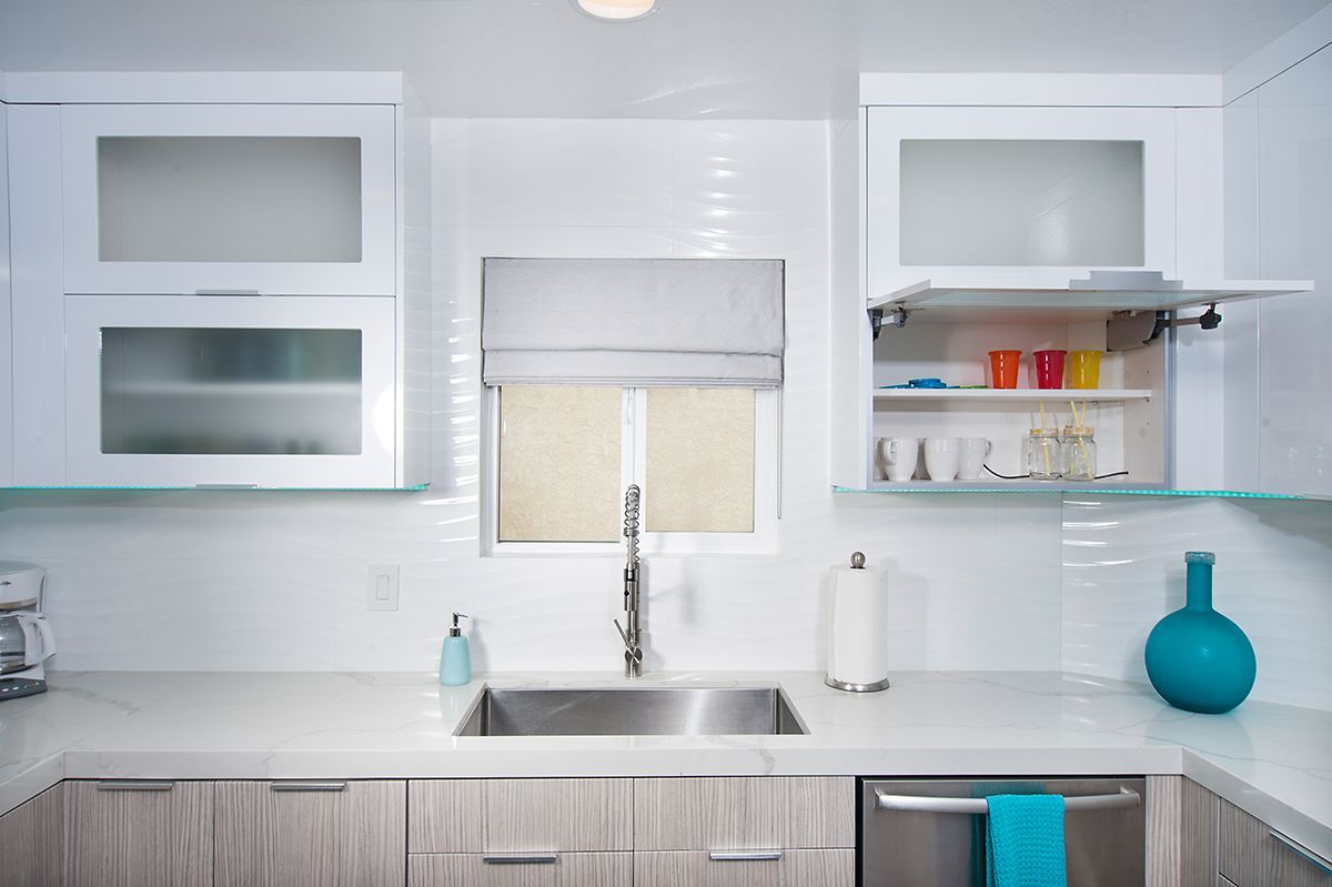 Modern white kitchen with cabinets, sink, and window. Light wood cabinets below the counter.