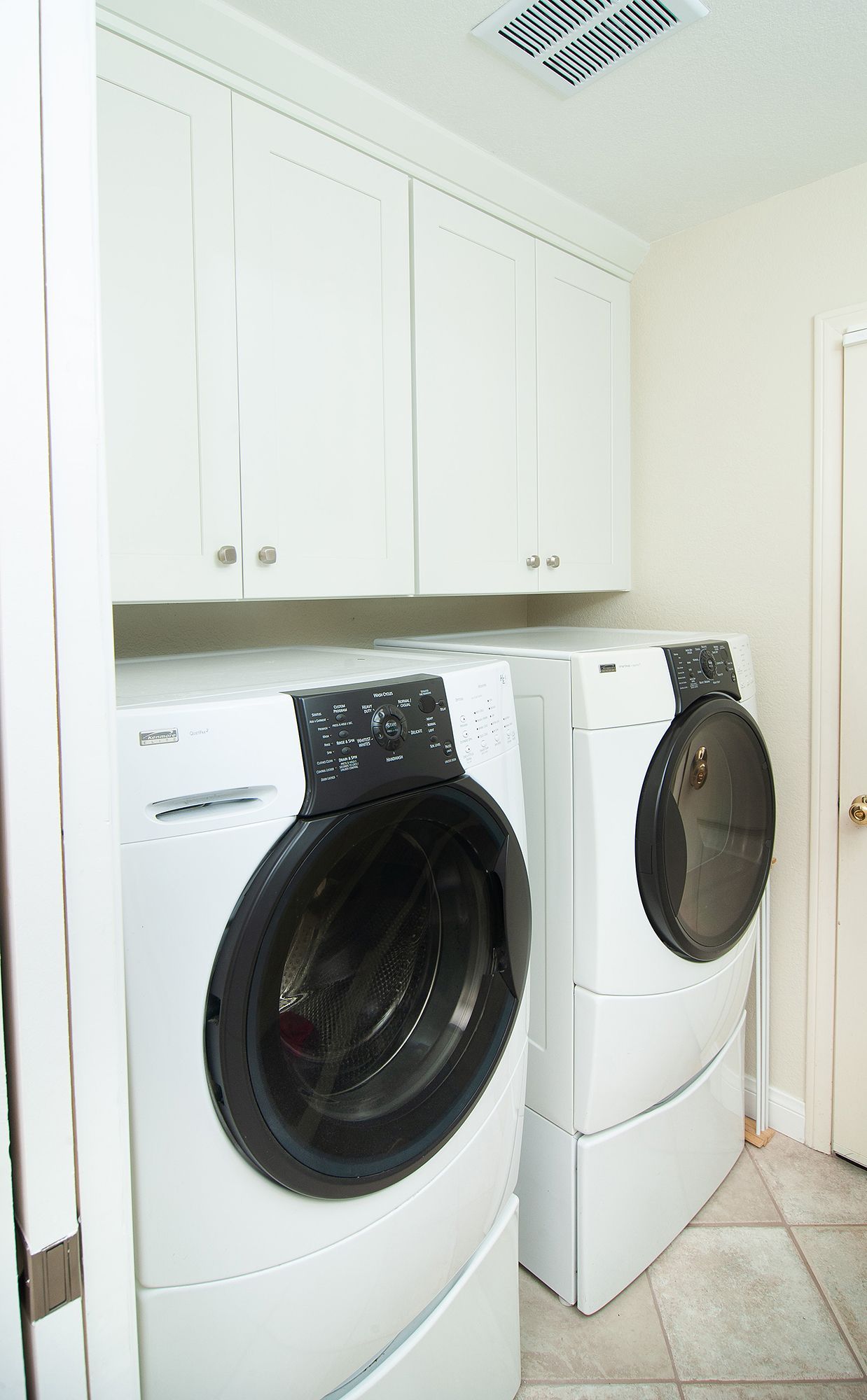 A white laundry room with a washer and dryer, white cabinets, and a closed door.