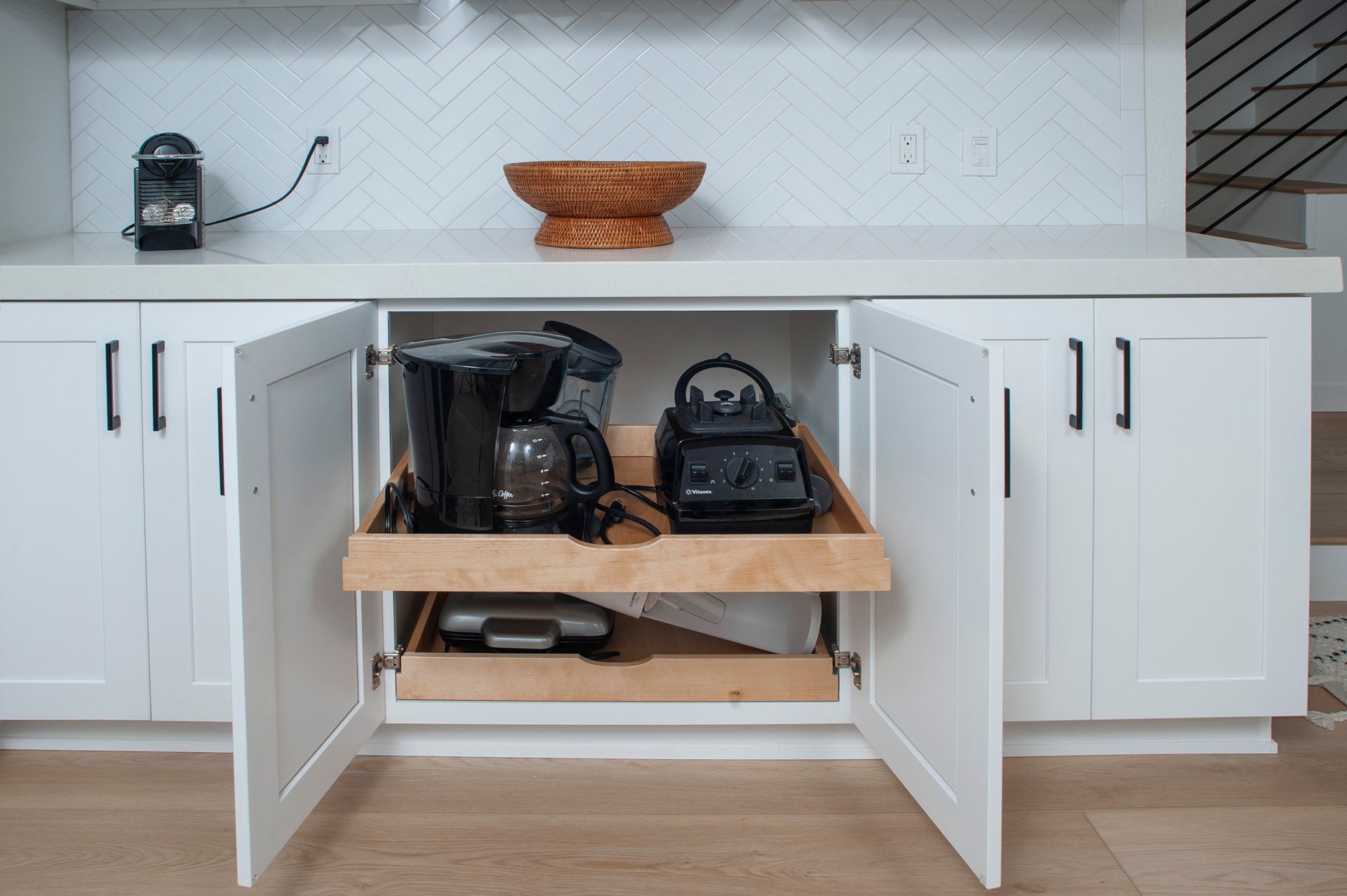 White kitchen cabinet open, revealing pull-out shelf with coffee maker, blender, and other appliances.