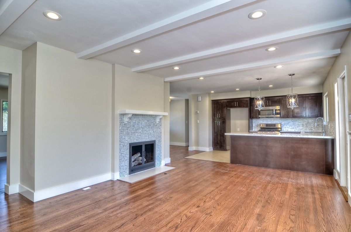 Living room with hardwood floors, fireplace, and open kitchen; neutral walls, dark cabinets.