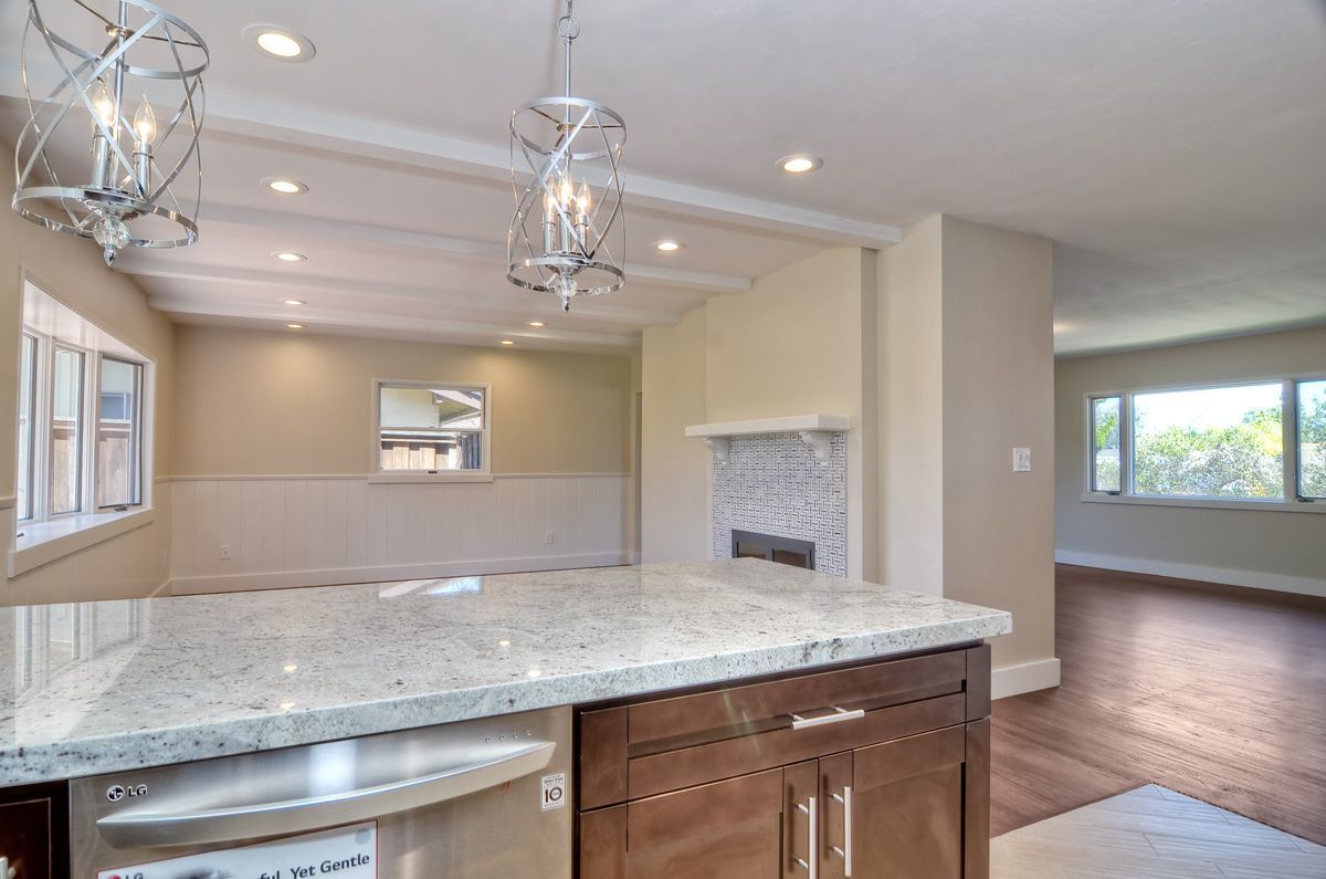 Kitchen with island, fireplace, and dining area; light-colored granite countertops, wooden cabinets and floors.