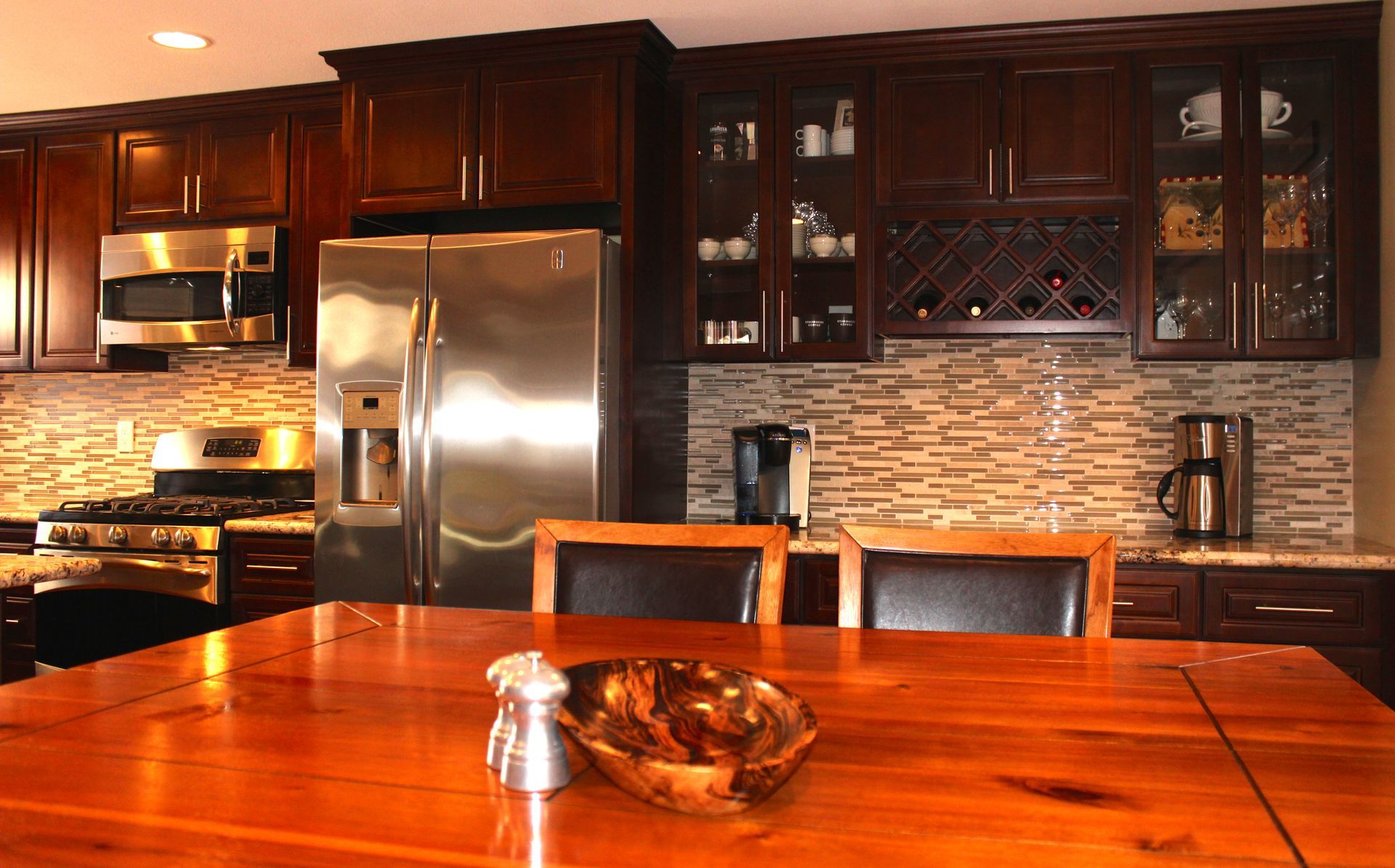Dark wood kitchen with stainless steel appliances, stone backsplash, and wood dining table.