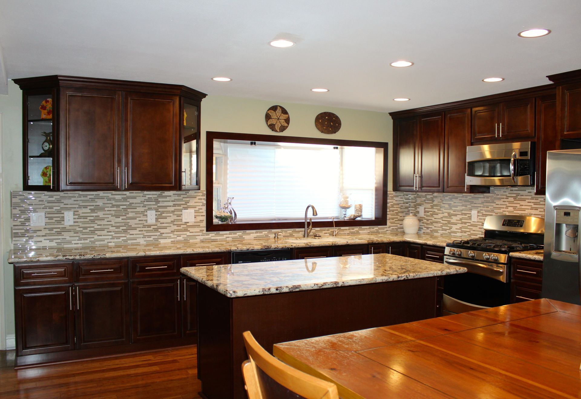 Dark wood kitchen with island, granite countertop, window, and stainless steel appliances.