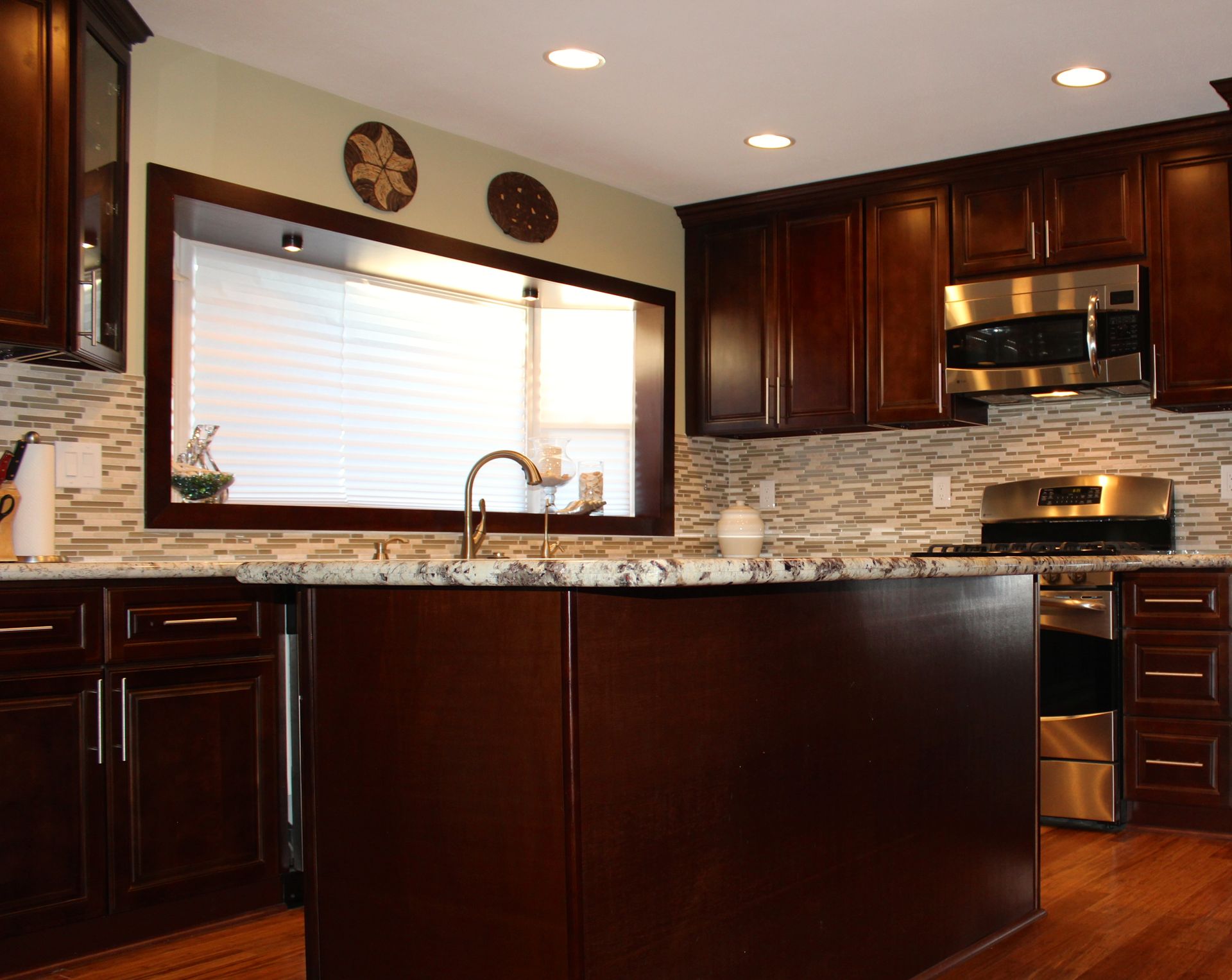 Kitchen with dark brown cabinets, island, stainless steel appliances, and window over sink.