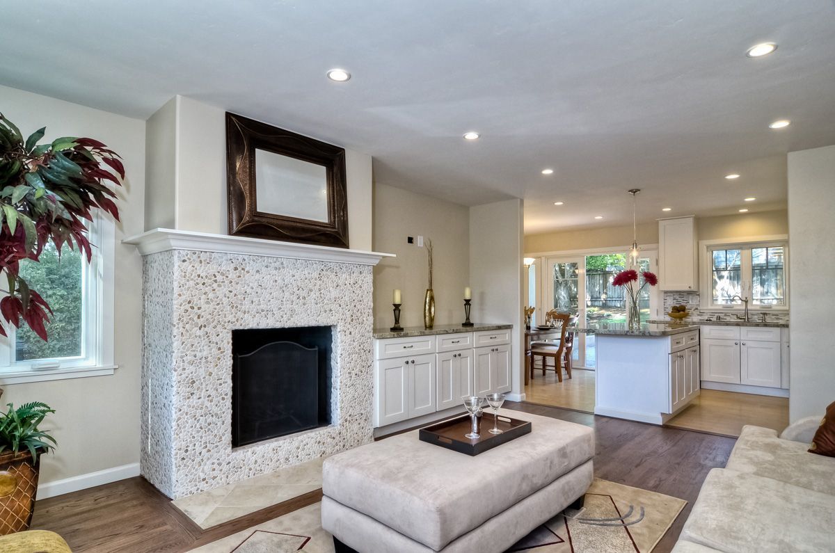 Living room with fireplace, built-in cabinets, and open kitchen, featuring beige walls, brown floors, and neutral furniture.