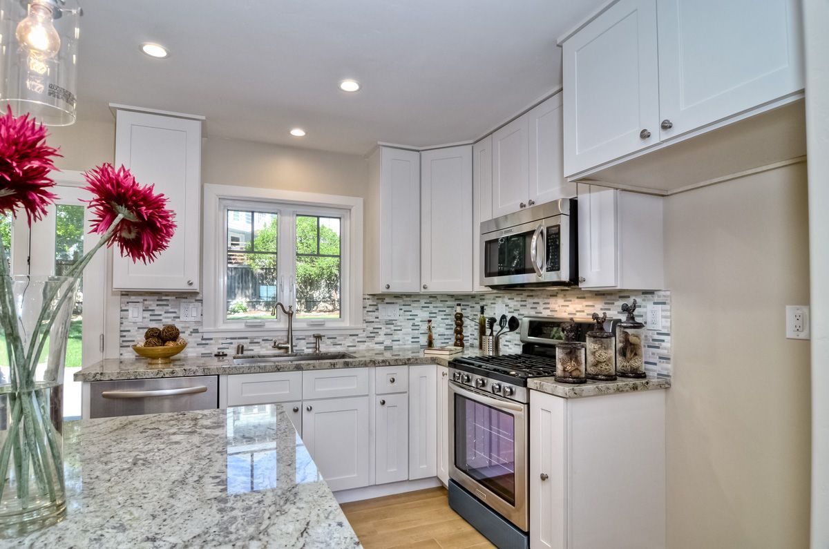 Bright white kitchen with granite countertops and stainless steel appliances.
