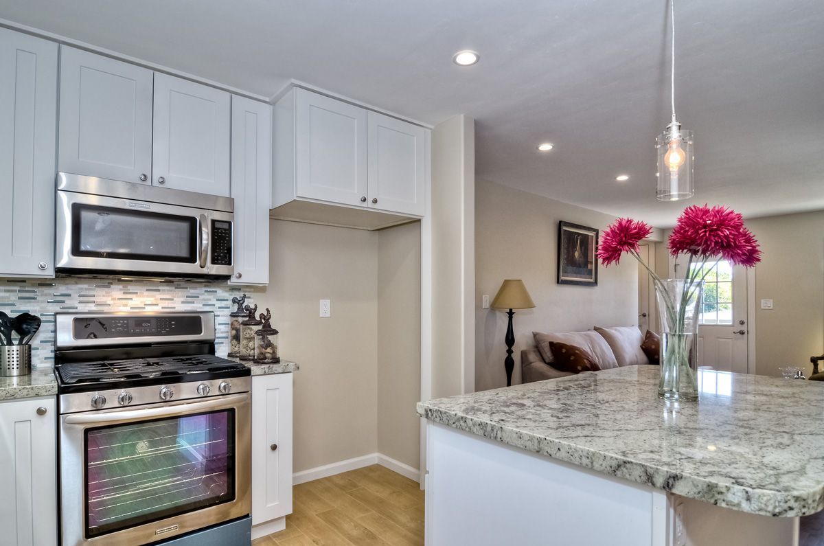 Kitchen with stainless steel appliances, white cabinets, granite countertop island, and bright pink flowers.