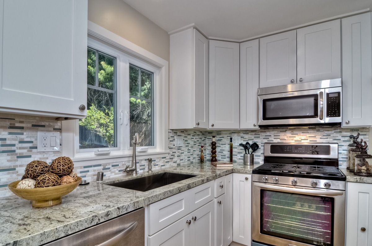 White kitchen with granite countertops, stainless steel appliances, and a window.