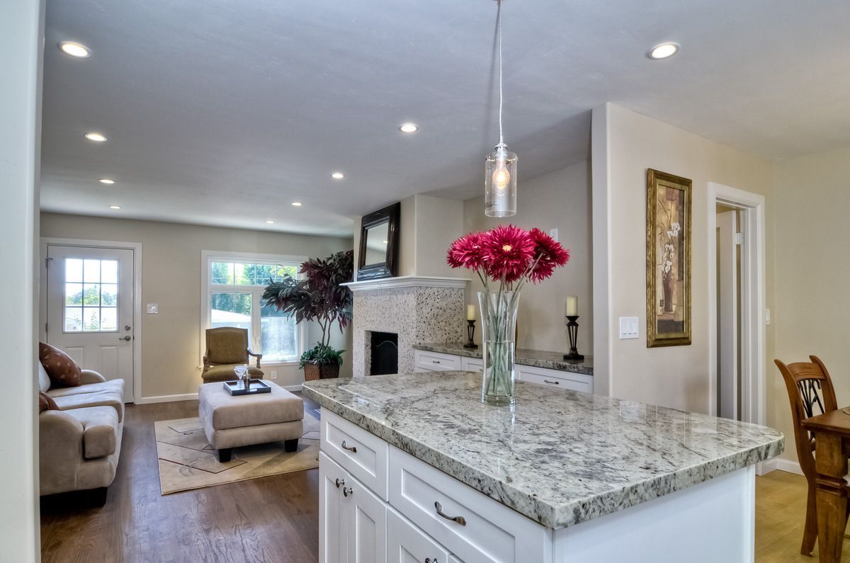 Open-concept kitchen with granite island, living room in the background with pink flowers in focus.