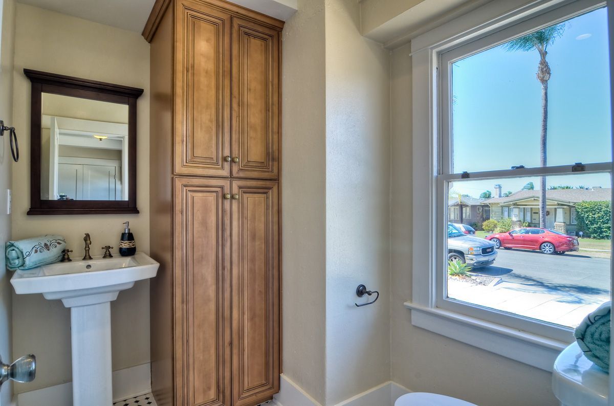 Bathroom with vanity, tall cabinet, and window overlooking a street with a red car.
