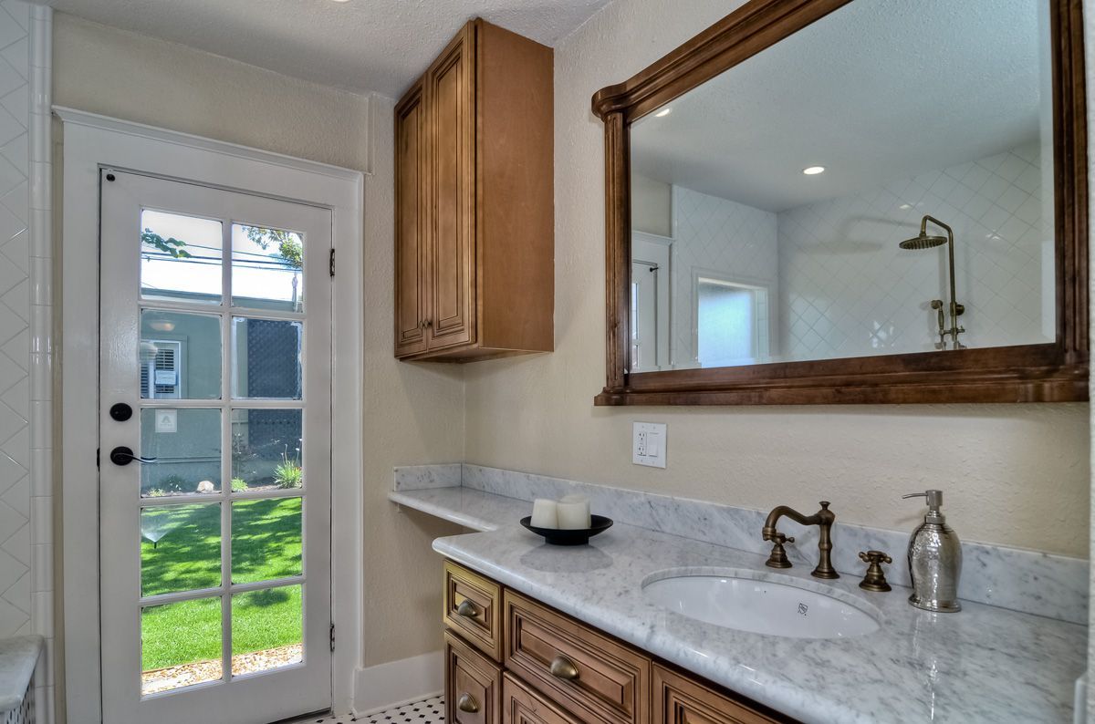 Bathroom with wooden vanity, marble countertop, large mirror, and door to a yard.