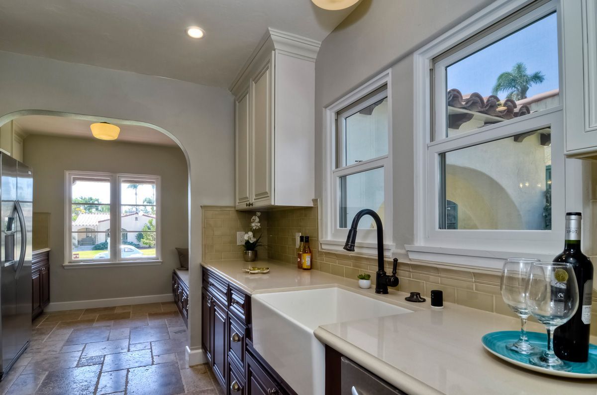 Kitchen with white cabinets, dark countertops, and a farmhouse sink. Windows reveal an exterior view.