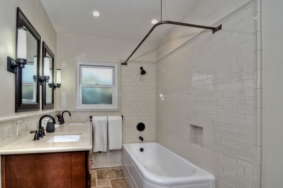 Bathroom with a white bathtub, white subway tile, and dark fixtures.