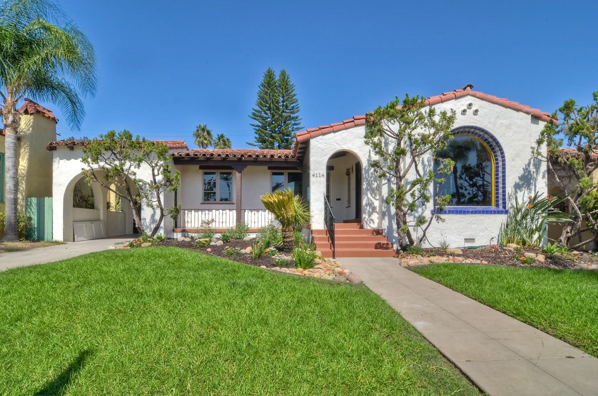 Spanish-style bungalow with white stucco, red tile roof, and lush green lawn.