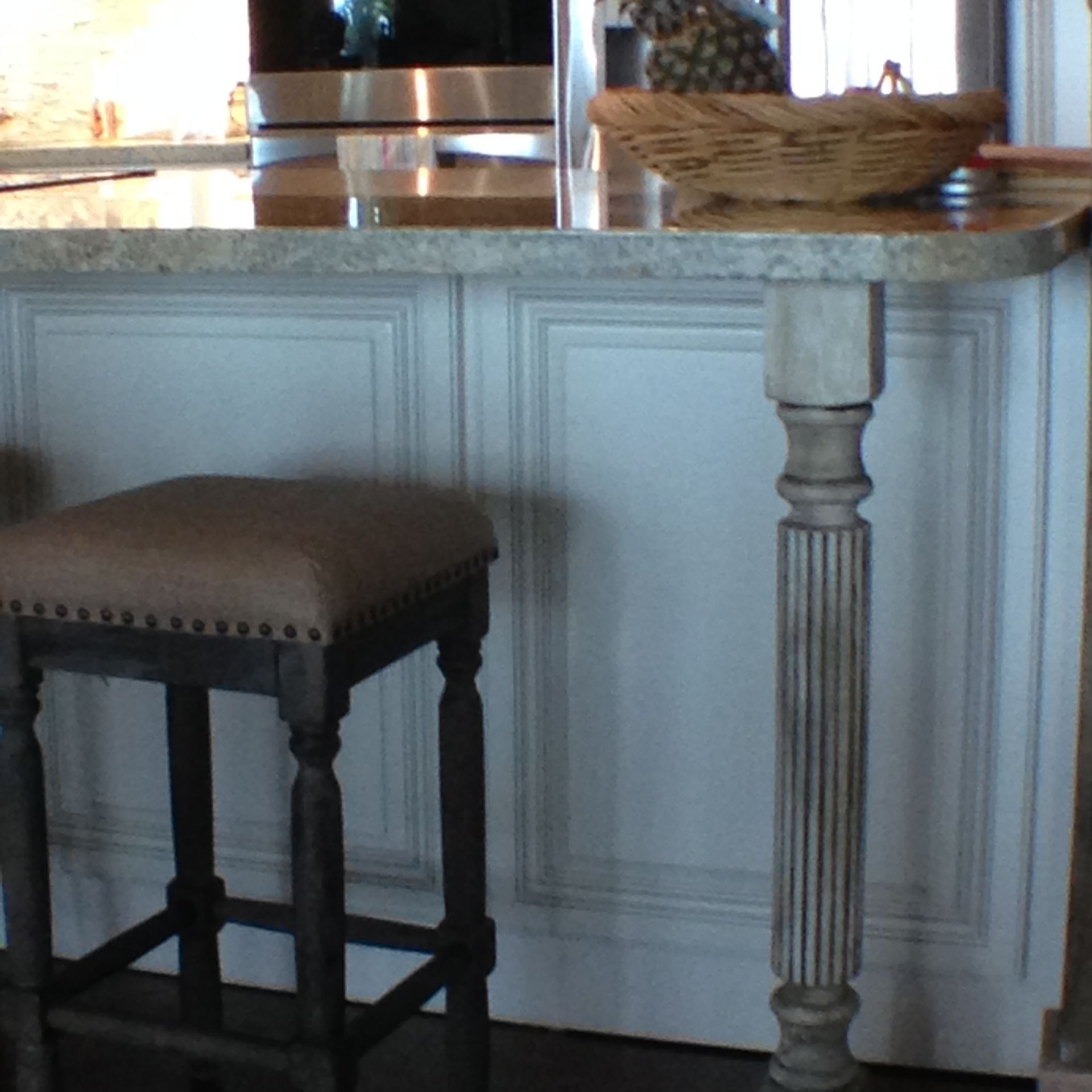 Kitchen island with a stool. Stool is brown with dark legs. Island has a marble top and white paneling.