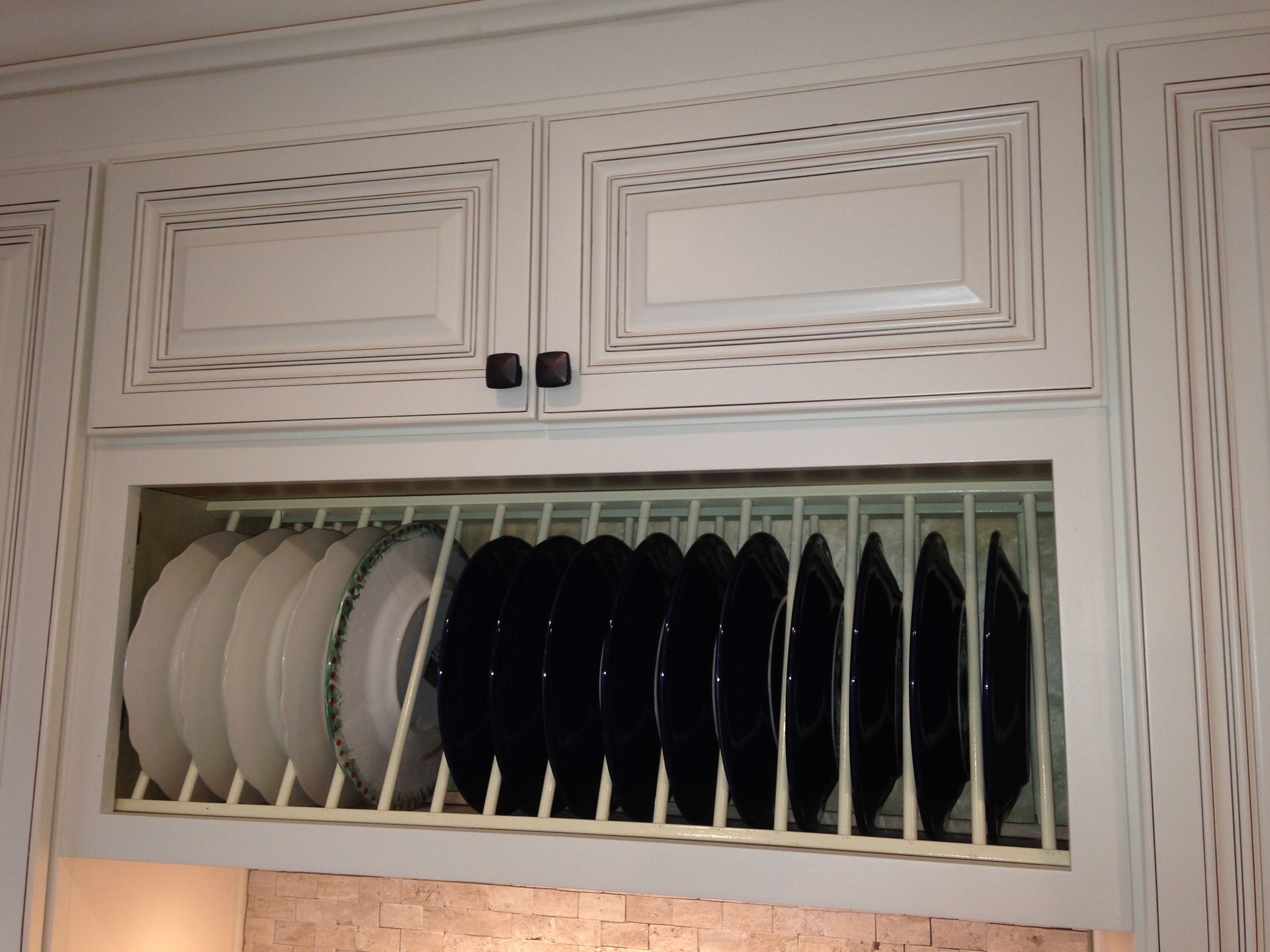 White kitchen cabinet with built-in dish rack holding white and black plates.