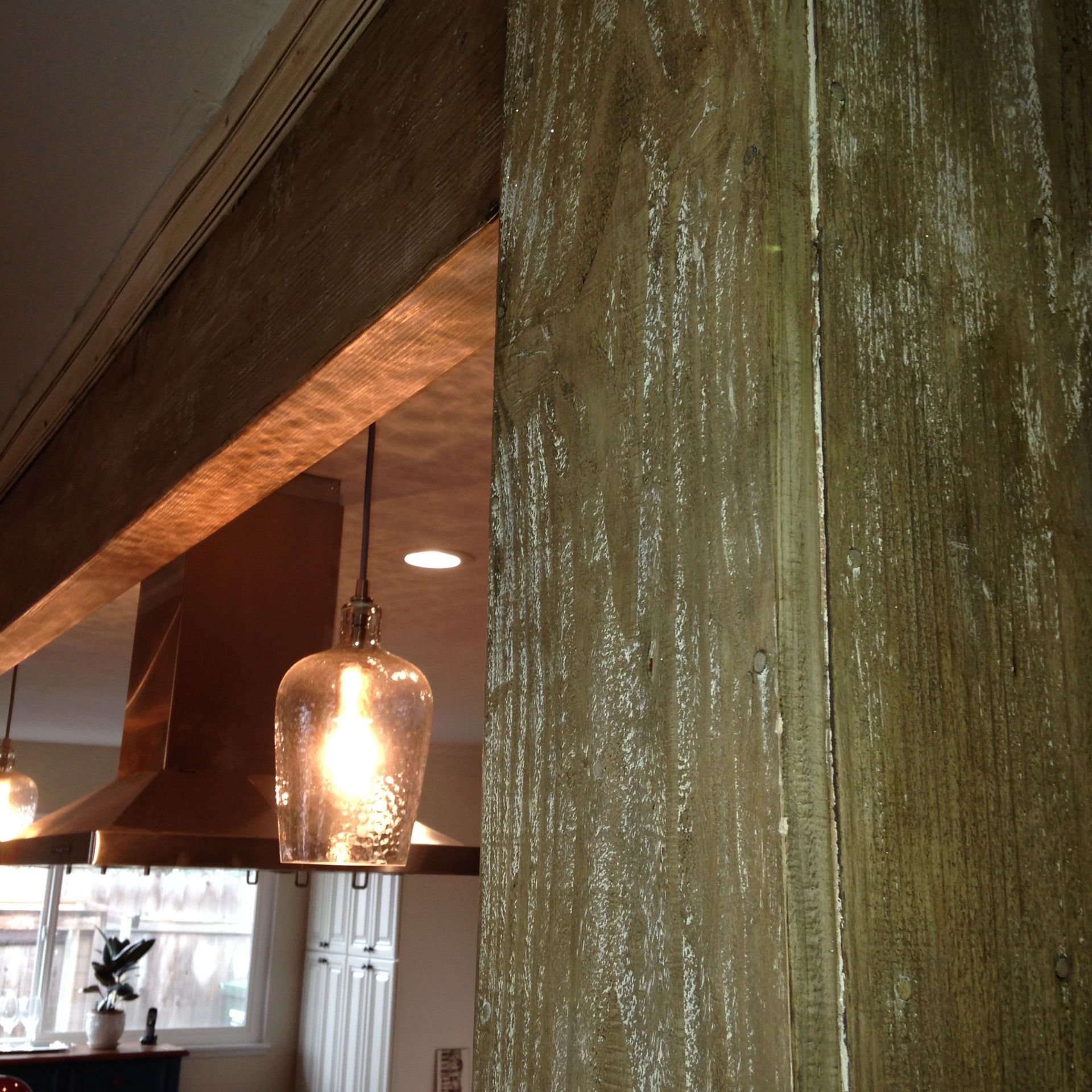 Wooden beams and pillars with hanging light fixtures in a kitchen.