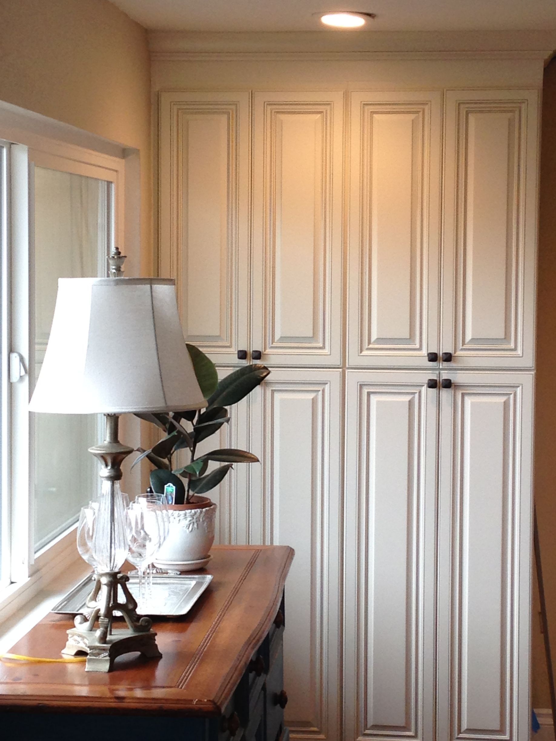 Cream cabinets and table with lamp and plant, by a window.