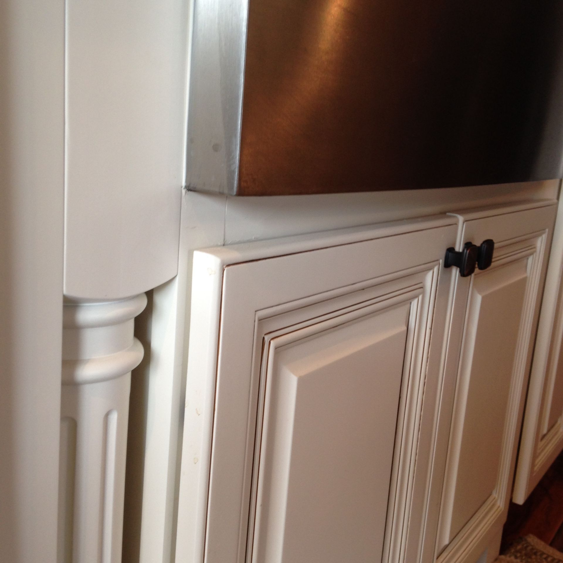 White kitchen cabinets and decorative pillar next to a stainless steel appliance.