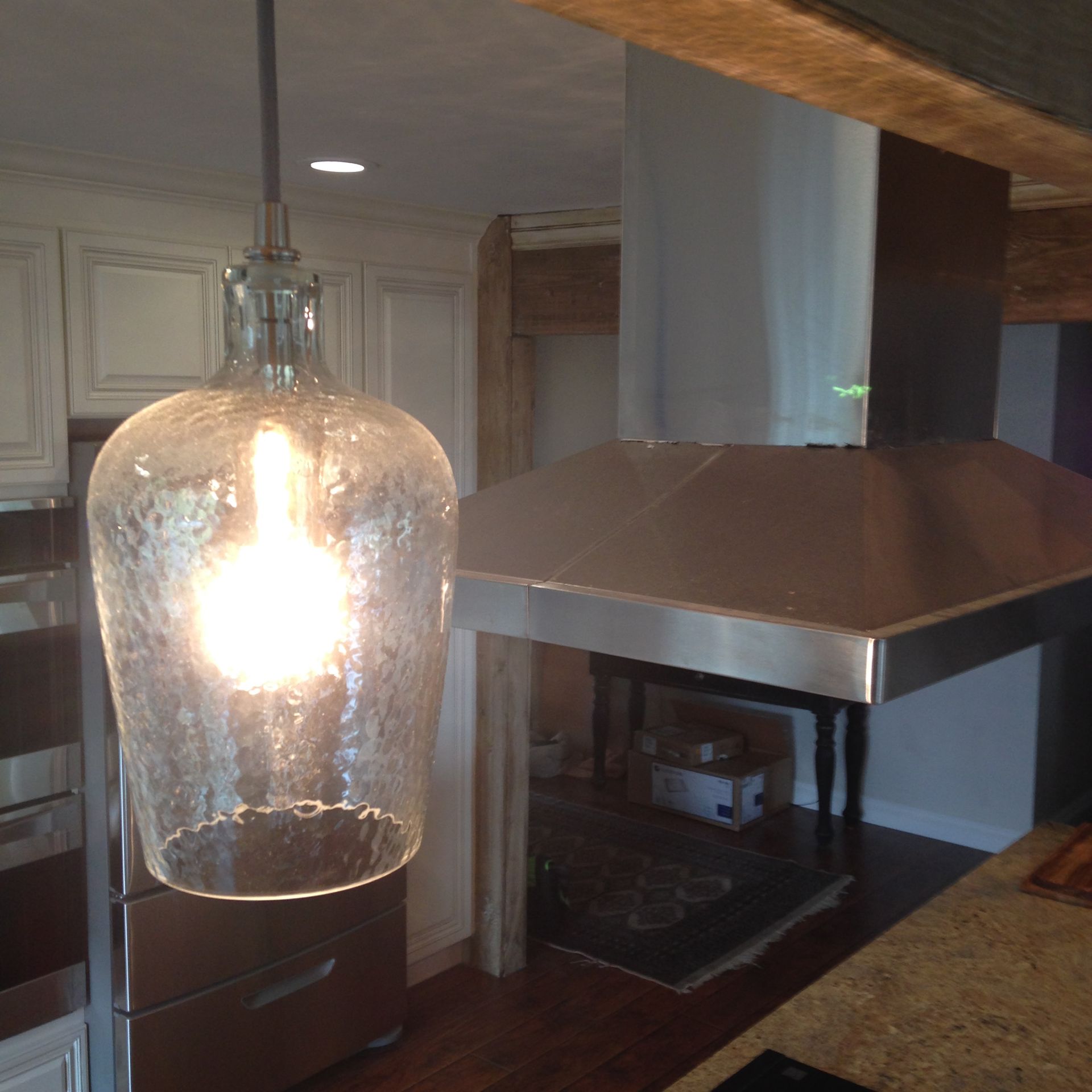 A glass pendant light illuminates a kitchen with a stainless steel range hood and white cabinets.