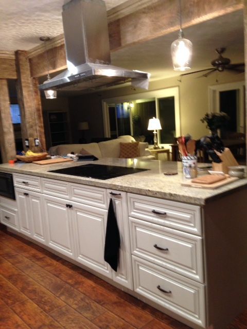 White kitchen island with cooktop, stainless steel vent hood, and view of a living room.