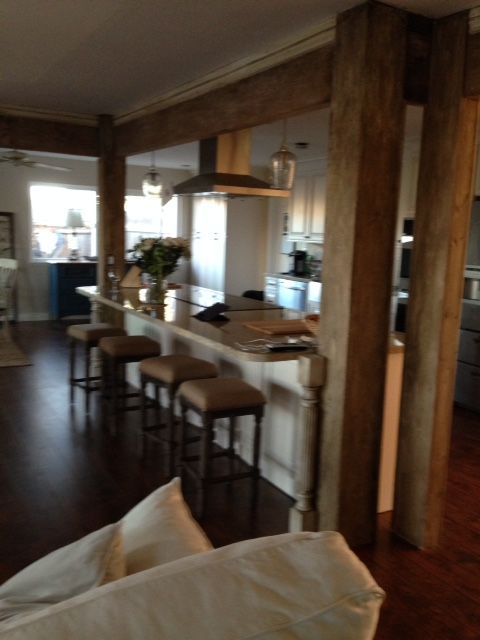 Kitchen with dark wooden beams, a white island with bar stools, and a stainless steel range hood.