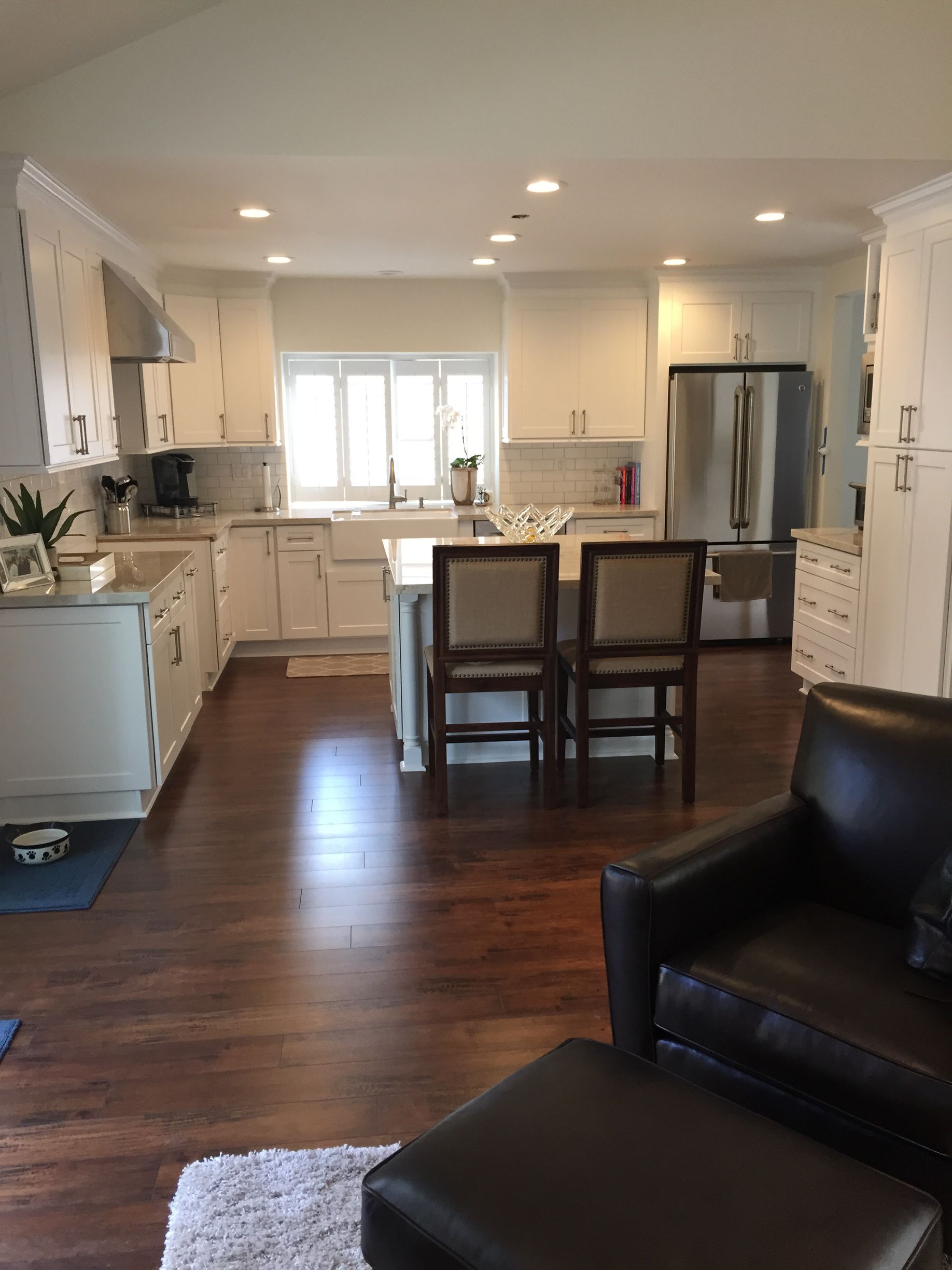 A kitchen with white cabinets and stainless steel appliances, dark wood floors, and bar seating.