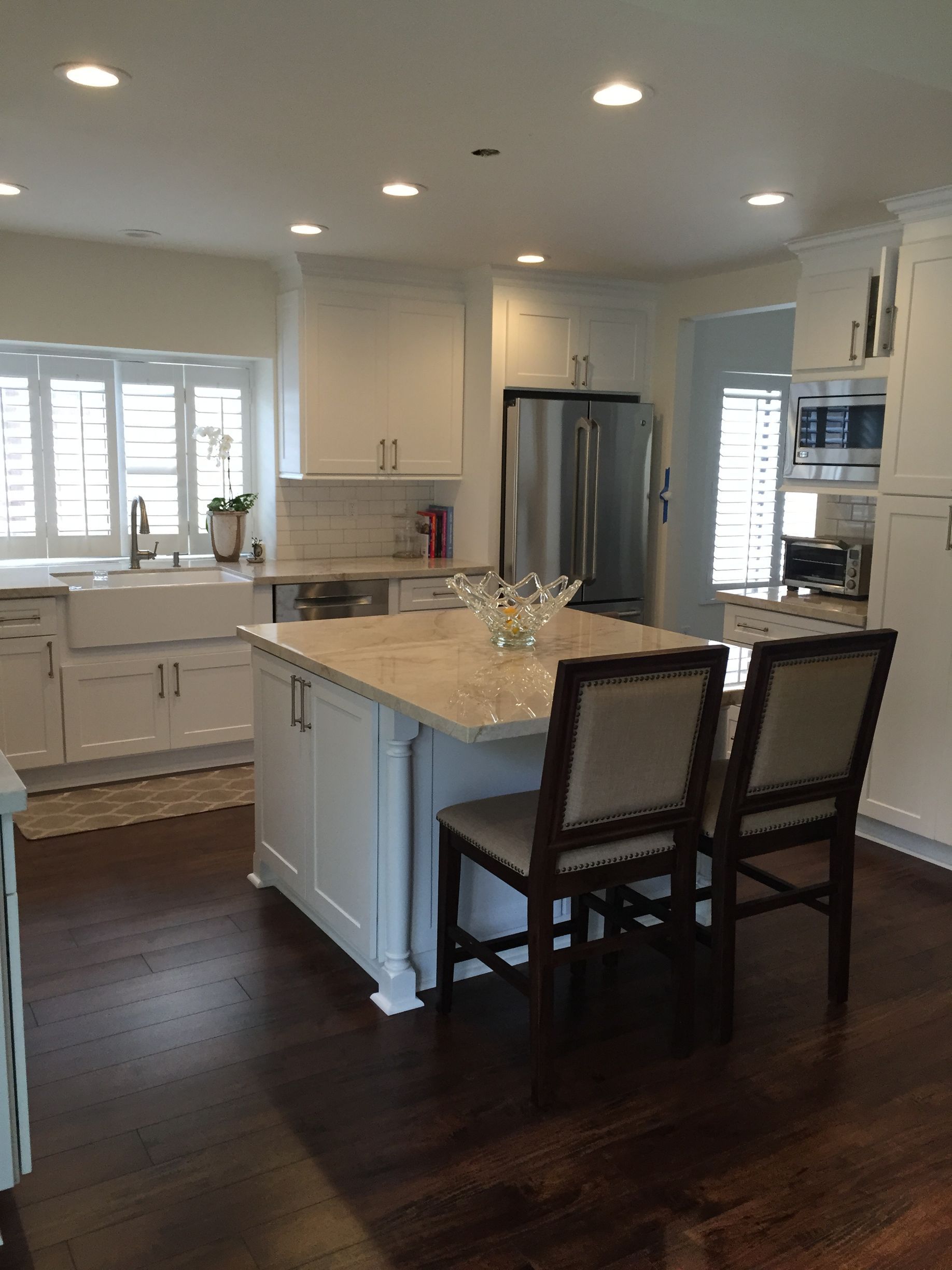 White kitchen with island, stainless steel appliances, dark wood floors, and two chairs.