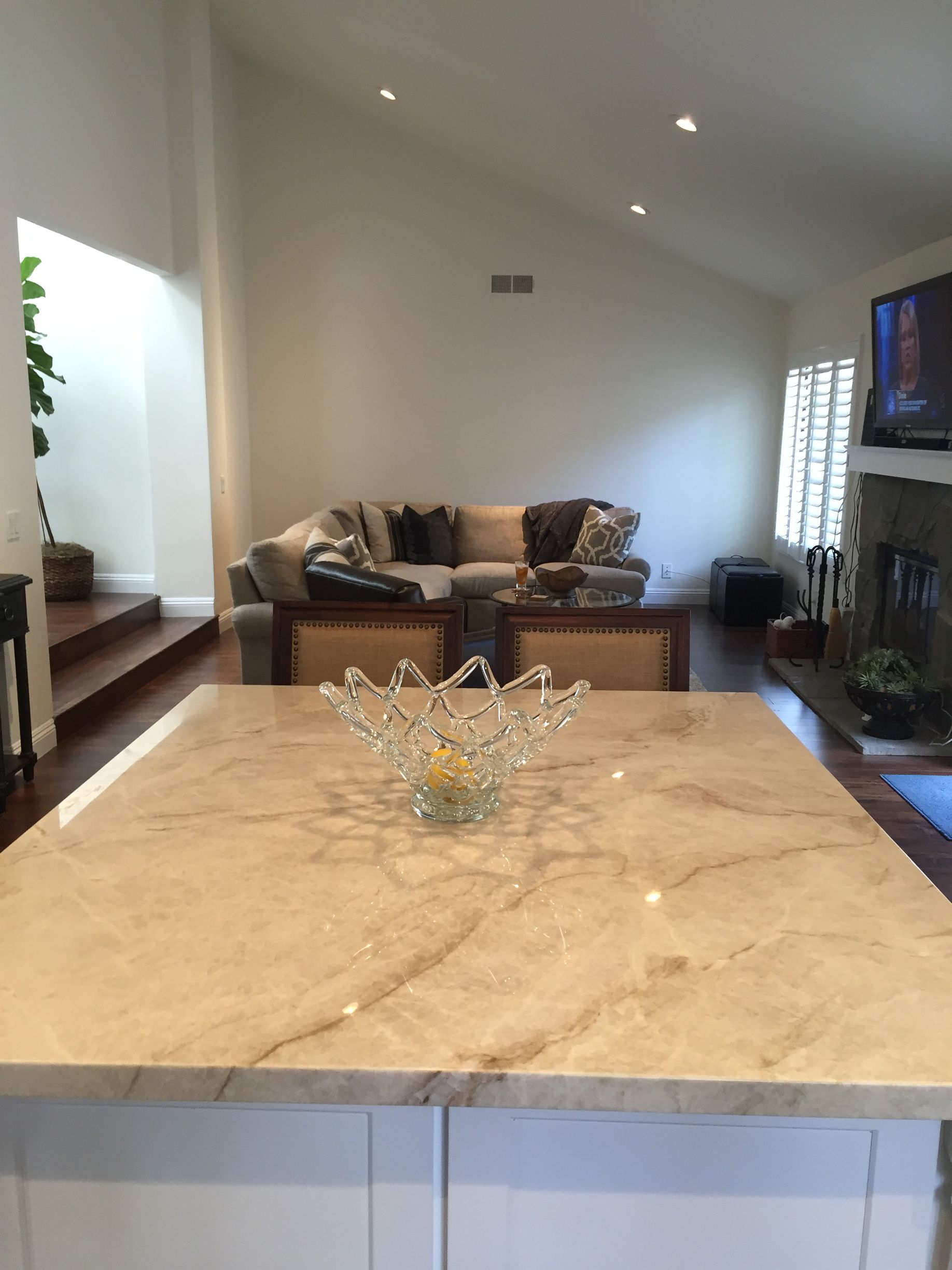 A modern kitchen island with marble countertop, a glass bowl, and a living room in the background.