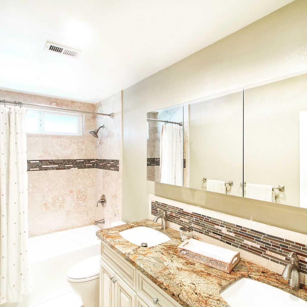Bathroom with a double sink vanity, bathtub with shower, and large mirror. Beige and brown tones.