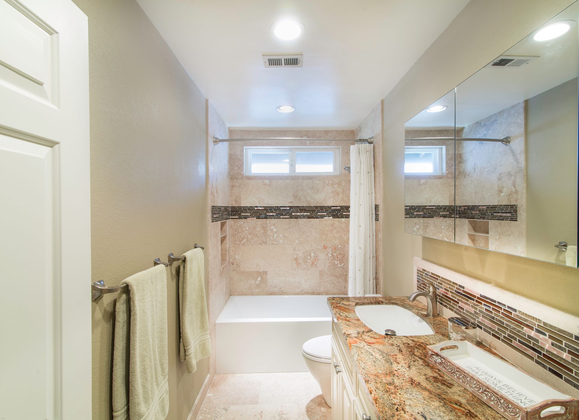 Bathroom with tub, sink, and toilet. Beige walls and granite countertop. Towels on rack.