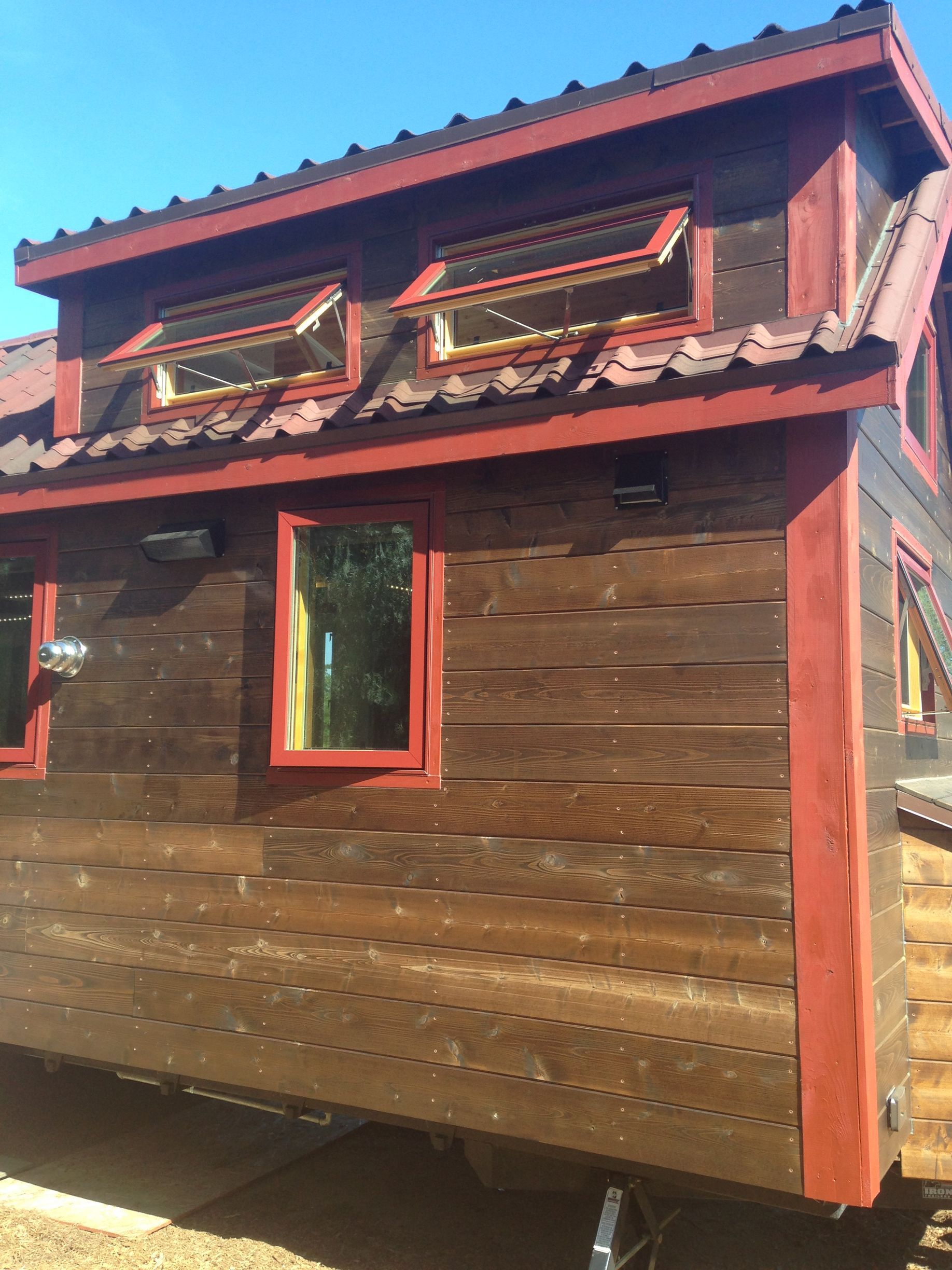 Tiny wooden house with red trim and windows under a blue sky.