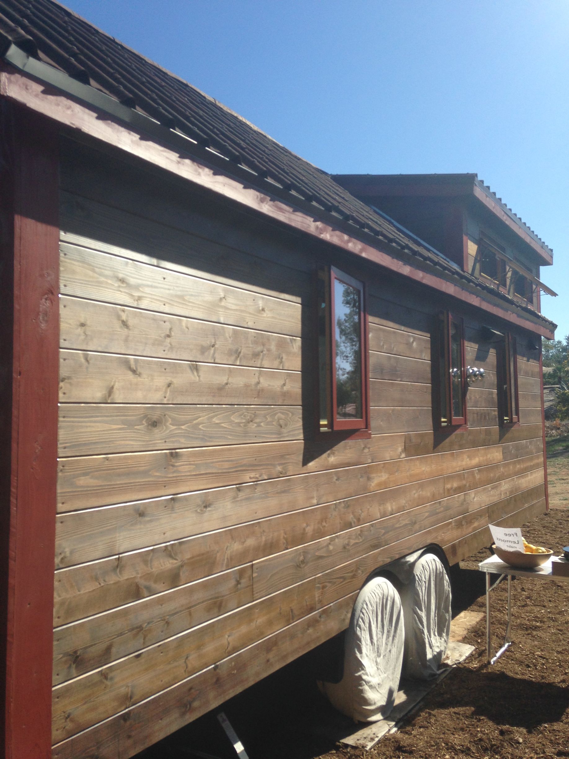 Side view of tiny house with wooden siding and red trim on a sunny day.